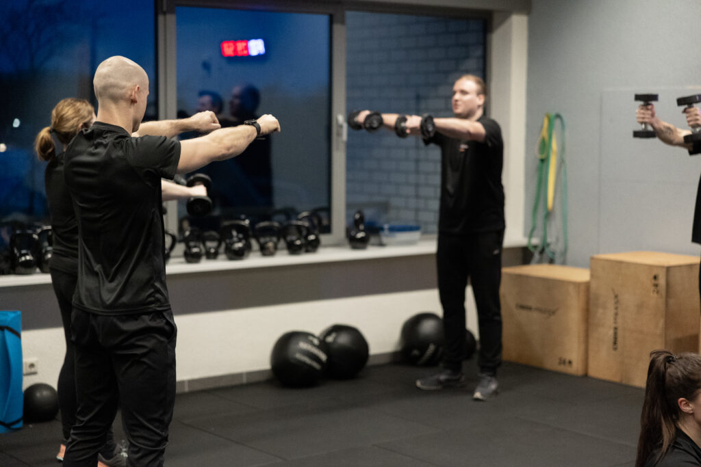 Coaches en deelnemers doen schouderoefeningen met dumbbells in groep bij Building You in Etten-Leur