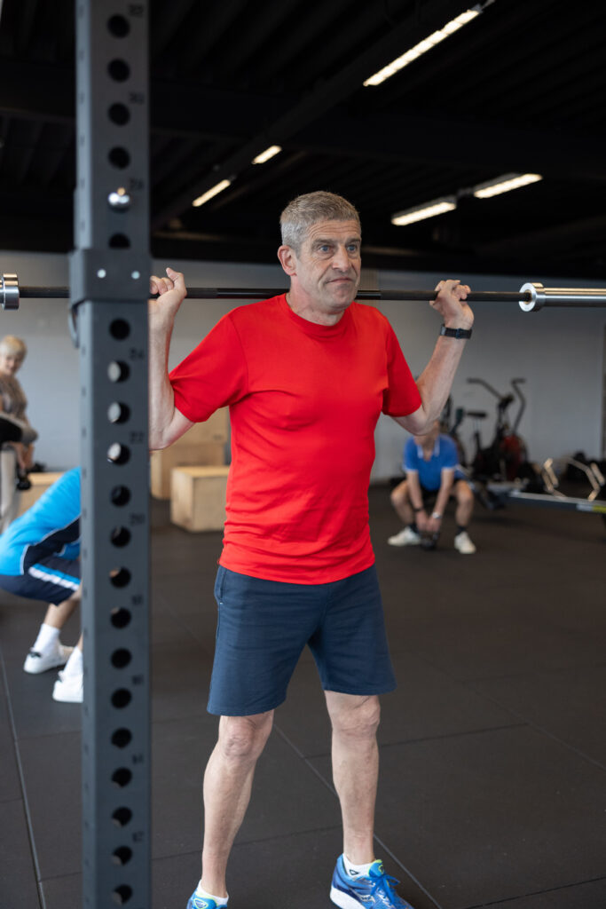 Man staat met een stang op de schouders in het rack tijdens krachttraining voor senioren bij Building You in Etten-Leur